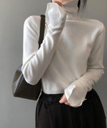 ホワイトのリブ編みハイネックニットを着た女性が、濃い茶色のボトムスを着用している写真。ニットの袖口はフレアのように広がるデザイン。