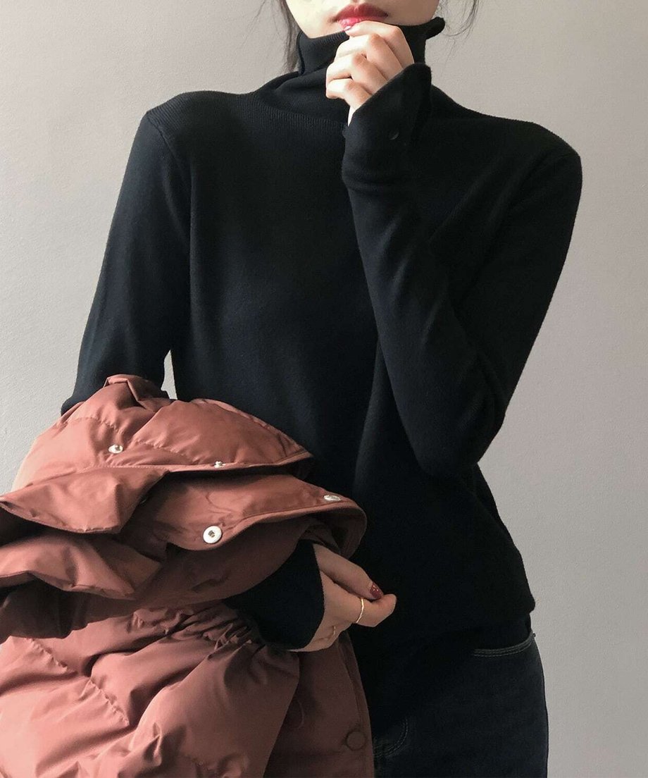 ブラックのハイネックリブニットを着用し、茶色のダウンジャケットを抱える女性の上半身。袖口のボタンディテールが見える。