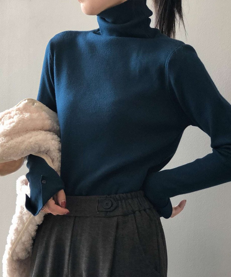 ブルーのハイネックニットを着用し、白いボアジャケットを持っている女性の上半身。
