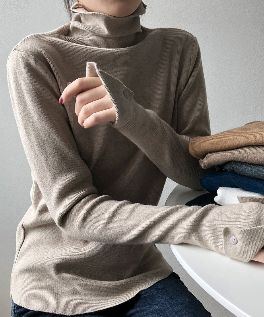 ミルクティーのリブハイネックニットを着用し、ジーンズと合わせた女性の全身。袖口のボタンディテールをクローズアップして見せている。