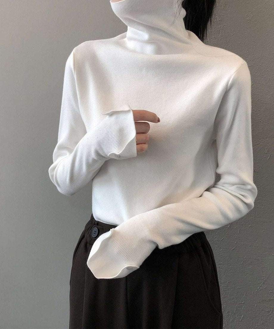 ホワイトのリブハイネックニットを着た女性が、濃い茶色のパンツを着用している写真。袖口を折り返し、指先が少し見えるようなデザイン。