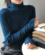 ブルーのハイネックリブニットを着用し、積み重ねられた多色のニットに手を添える女性のバストアップ。