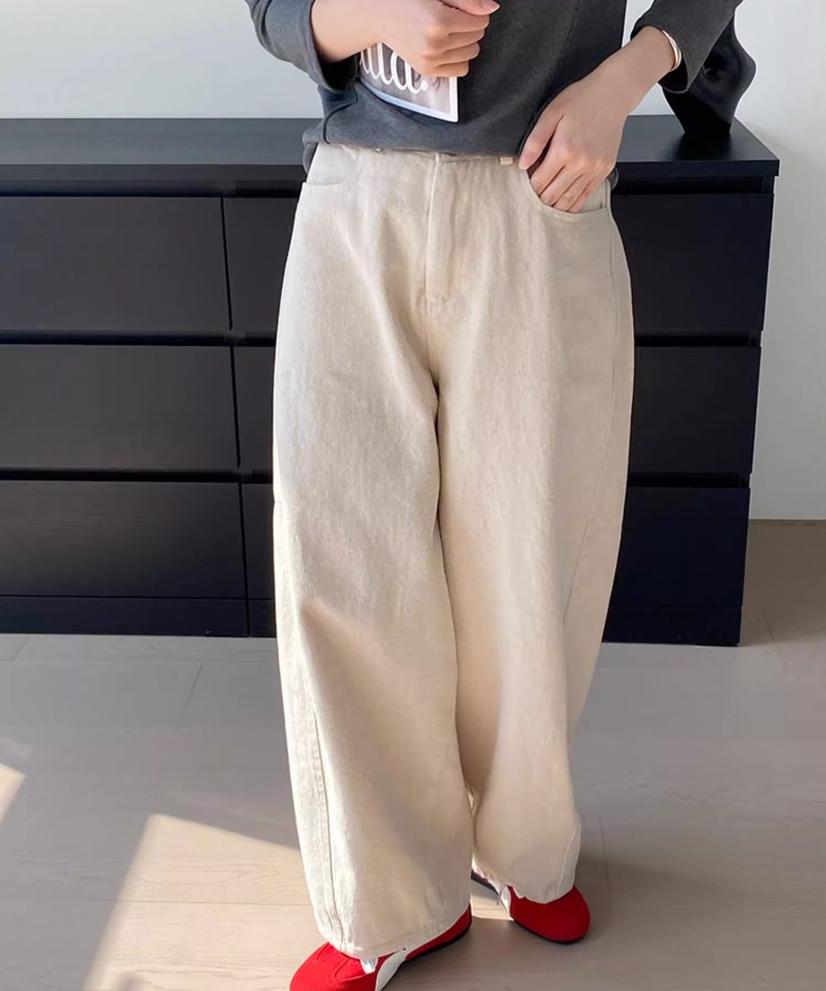  アイボリーのワイドパンツとチャコールグレーの長袖Tシャツを着た女性が座って雑誌を持っているクローズアップ写真。