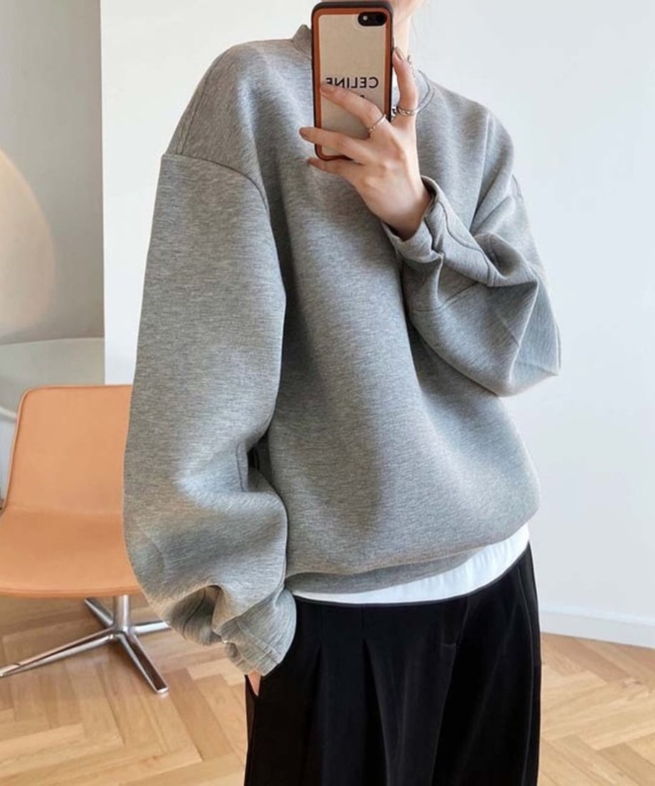 グレーのオーバーサイズスウェットを、白いインナーTシャツと黒のボトムスにレイヤードして着用している女性の写真。