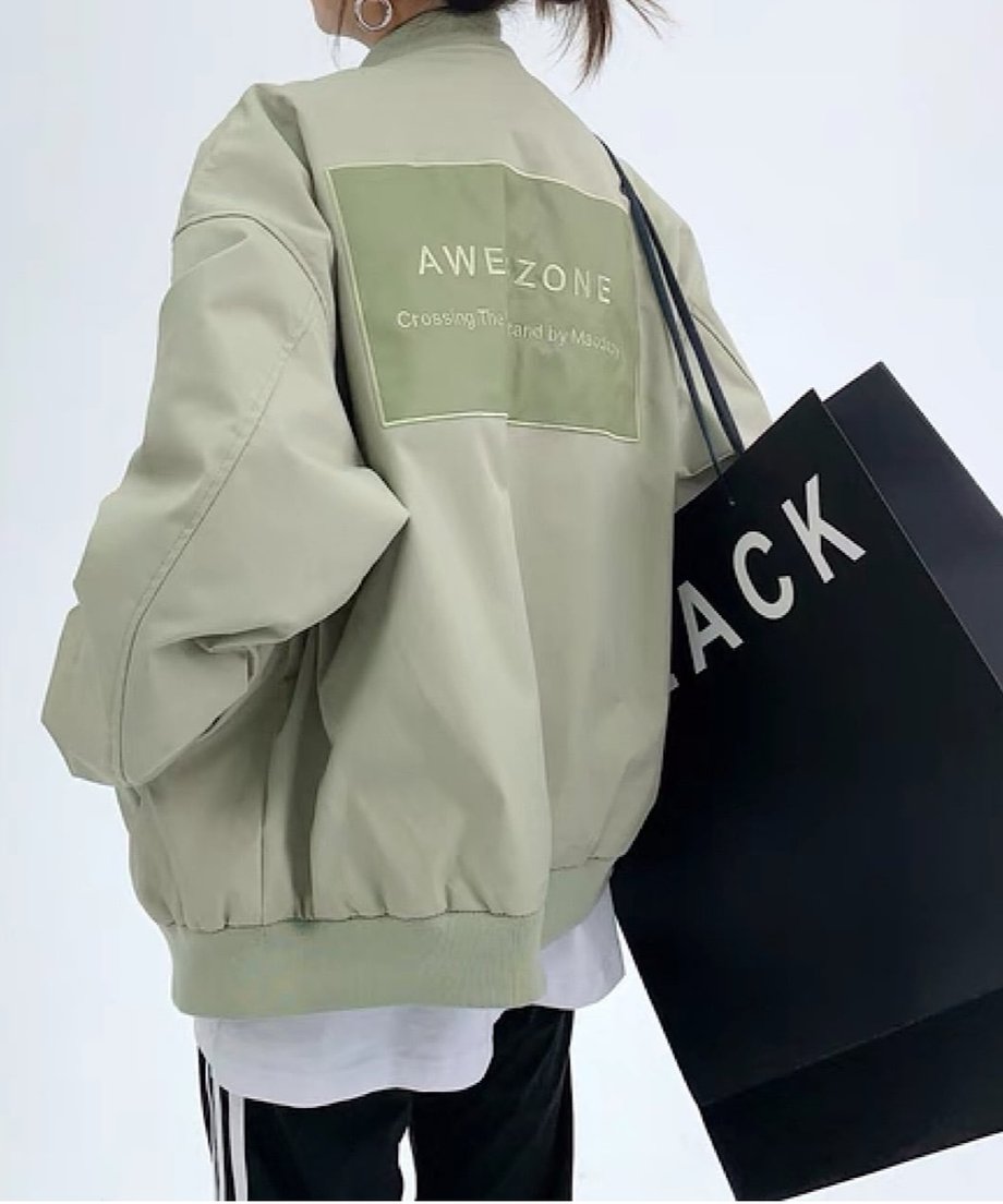 ライトグリーンのオーバーサイズボンバージャケットを着用した後ろ姿。背中に大きな長方形のロゴプリントが施されたストリートデザイン。