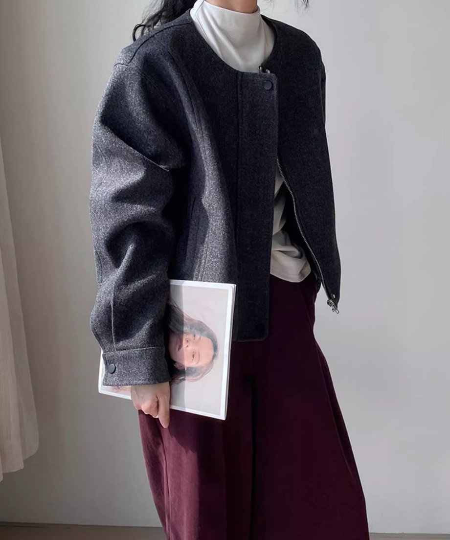 グレーのノーカラージャケットを着用した女性の全身写真。白のハイネックインナーとワインレッドのワイドパンツを合わせたシックな秋コーデ。手に雑誌を持っている。