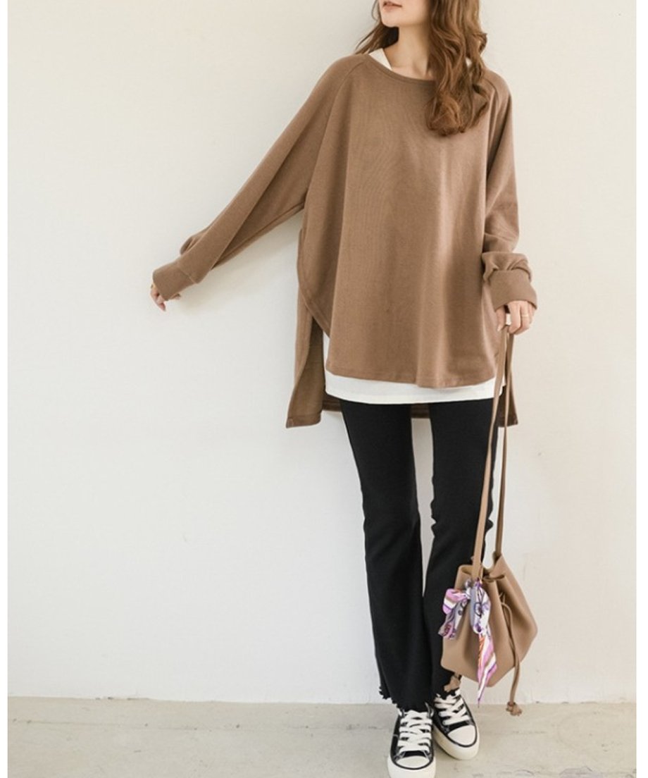 モカのオーバーサイズニットを着用した女性の全身画像。黒いフレアパンツとスニーカーを合わせたコーディネート。