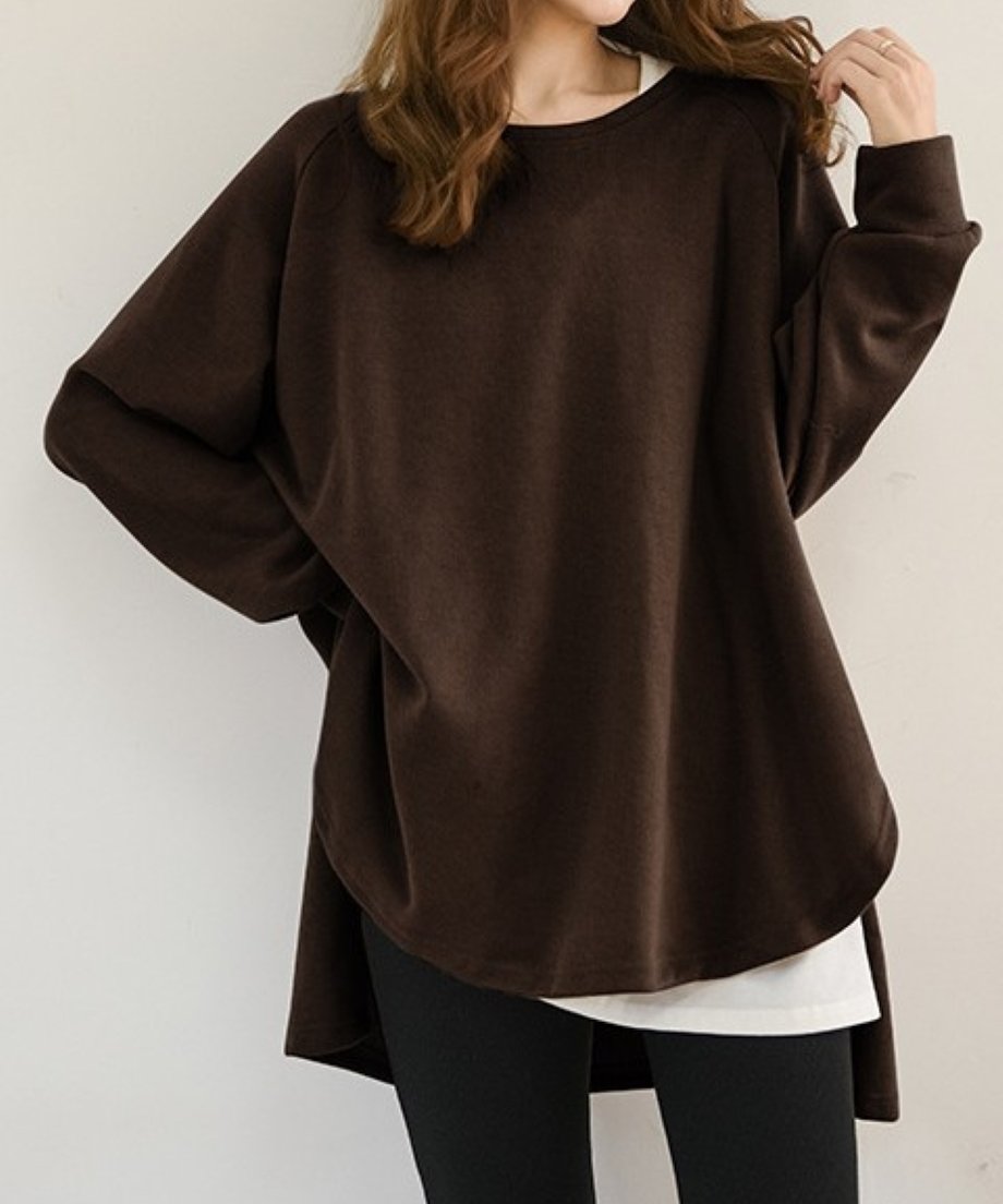 コーヒーのオーバーサイズニットを着用した女性のミドルショット。横から見た時の裾の前後差のあるデザインが確認できる。