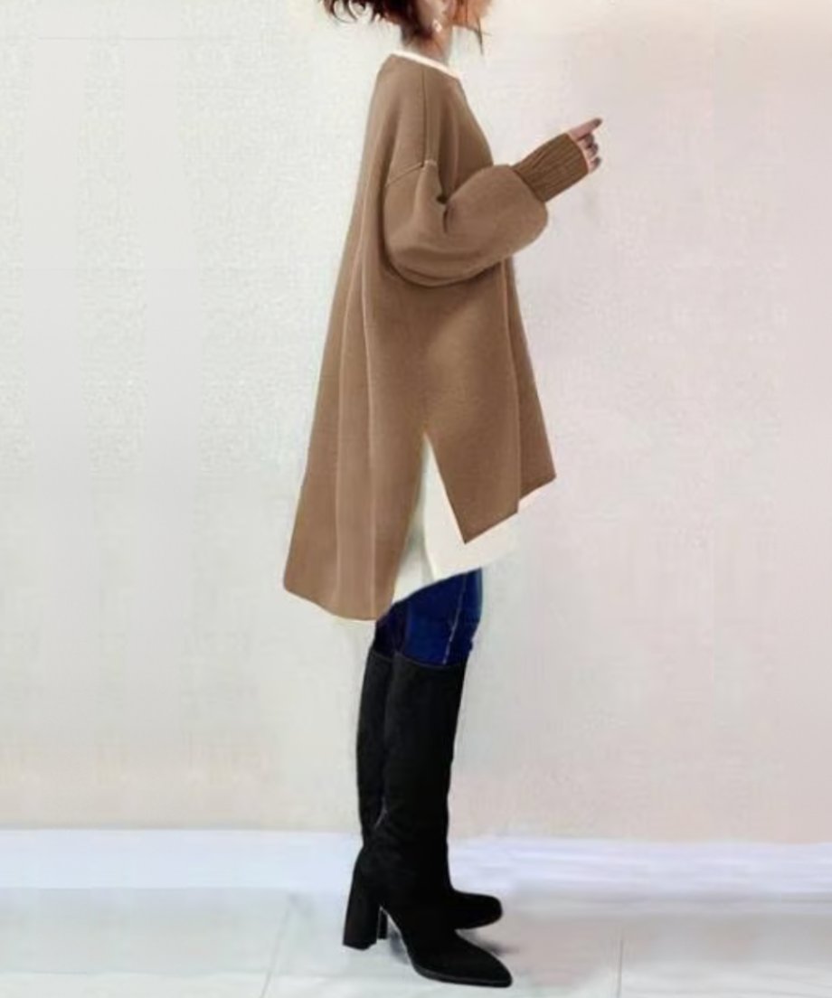 カーキののポンチョ風オーバーサイズトップスを着用した女性の全身サイドビュー。流れるような裾のラインとサイドスリット、黒いロングブーツが確認できる。