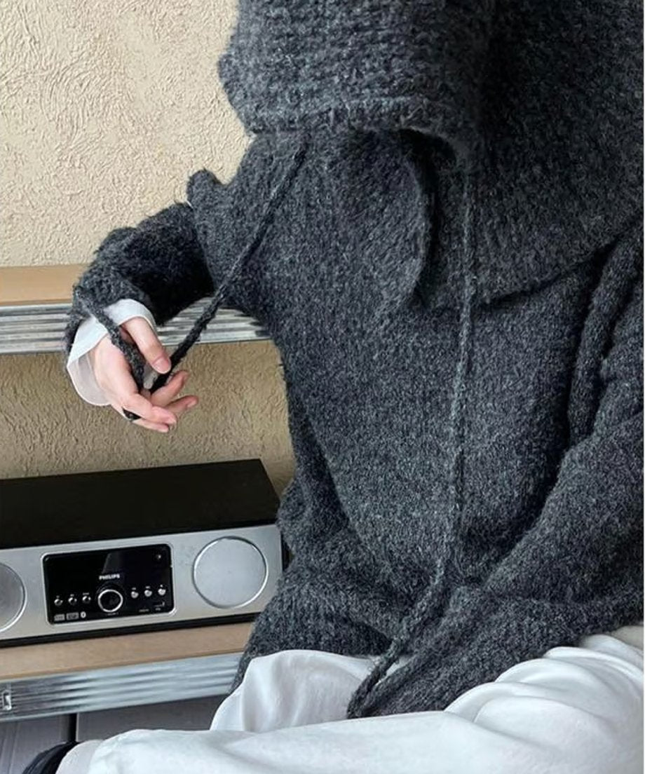 グレーのざっくりニットを着用した女性のクローズアップ。白のインナーとボトムスを合わせたリラックスした着こなし。