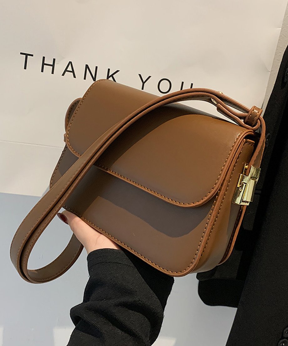 ブラウンのフェイクレザーショルダーバッグを黒いジャケットの上で手に持っている写真。背景に「THANK YOU」の文字が見える。