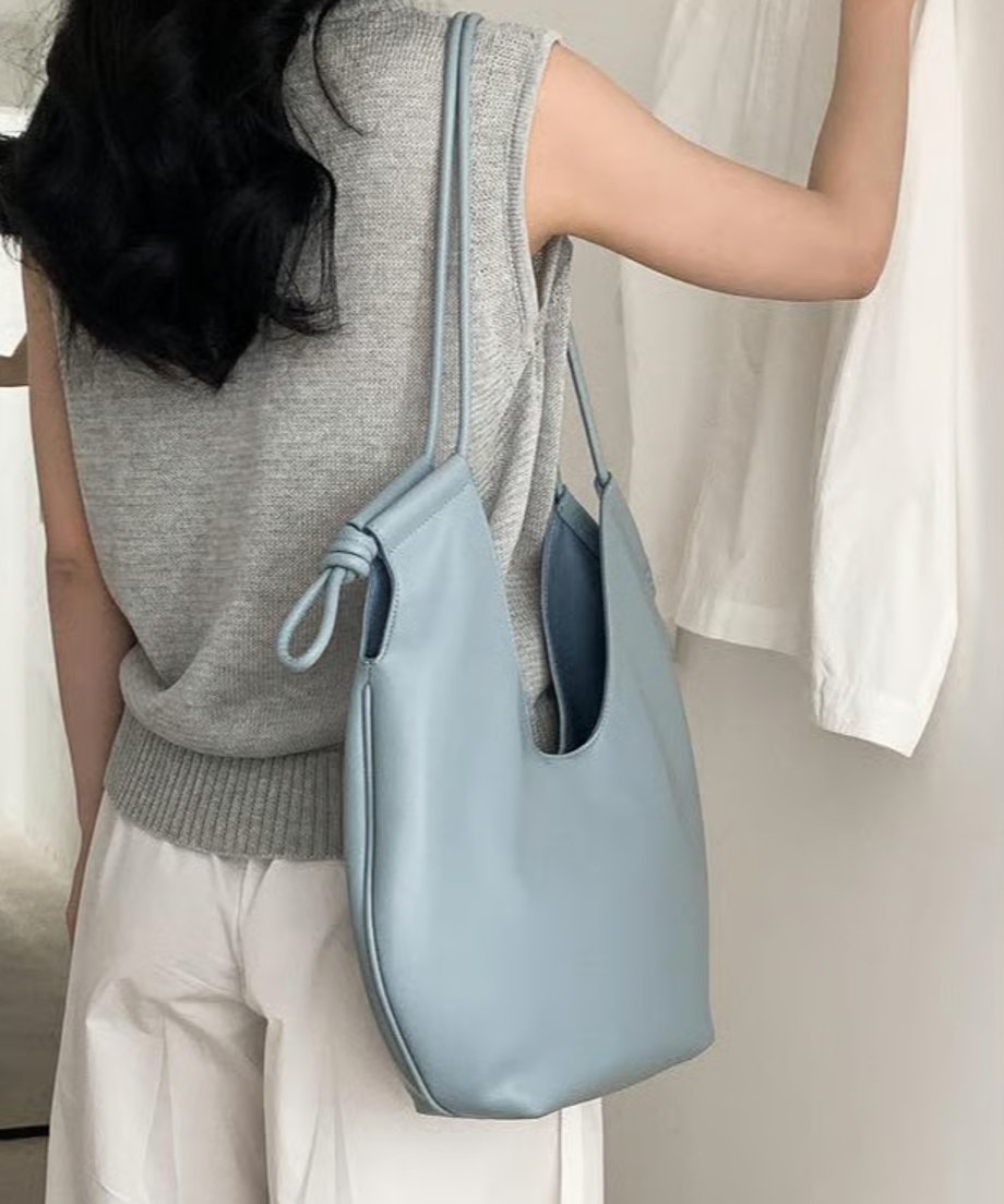 色のノースリーブと白いワイドパンツを着用した女性が、ライトブルーのノットデザインショルダーバッグを肩にかけている後ろ姿。