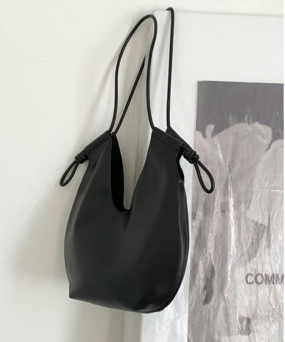 白い壁を背景に、黒色のノットデザインショルダーバッグが吊り下げられている商品単体画像。