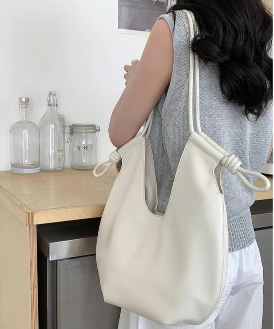 色のノースリーブと白いワイドパンツを着用した女性が、ホワイトのノットデザインショルダーバッグを肩にかけている後ろ姿