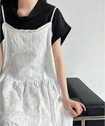 黒いTシャツに白い刺繍キャミソールワンピースを重ね着した女性のバストアップ。