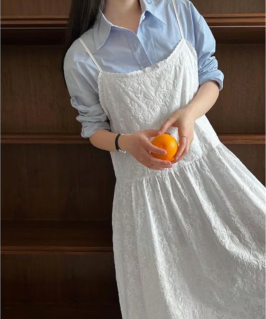 水色の長袖シャツに白い刺繍キャミソールワンピースを重ね着し、みかんを持っている女性のバストアップ。