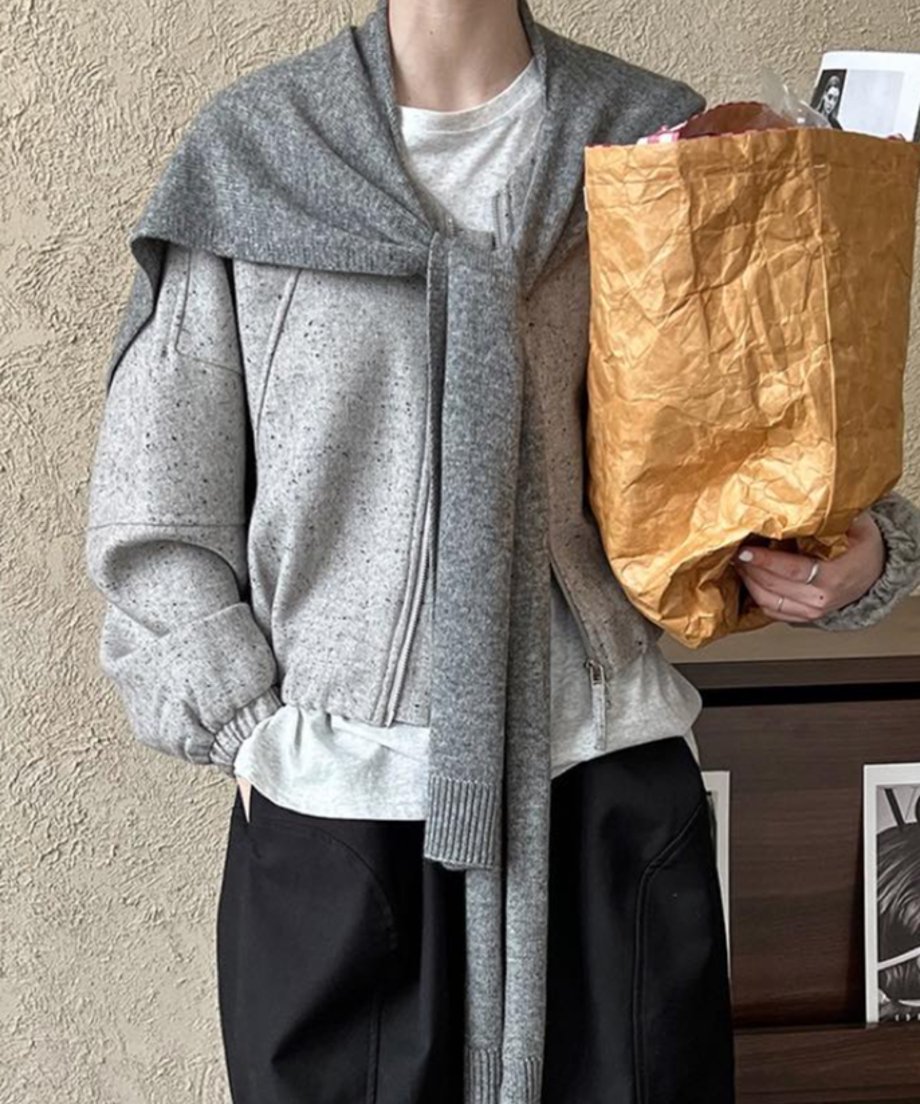 グレーのデザインジャケットと同系色のニットストールを肩掛けし、チェック柄の裏地が見える茶色の紙袋型バッグを持っている女性。