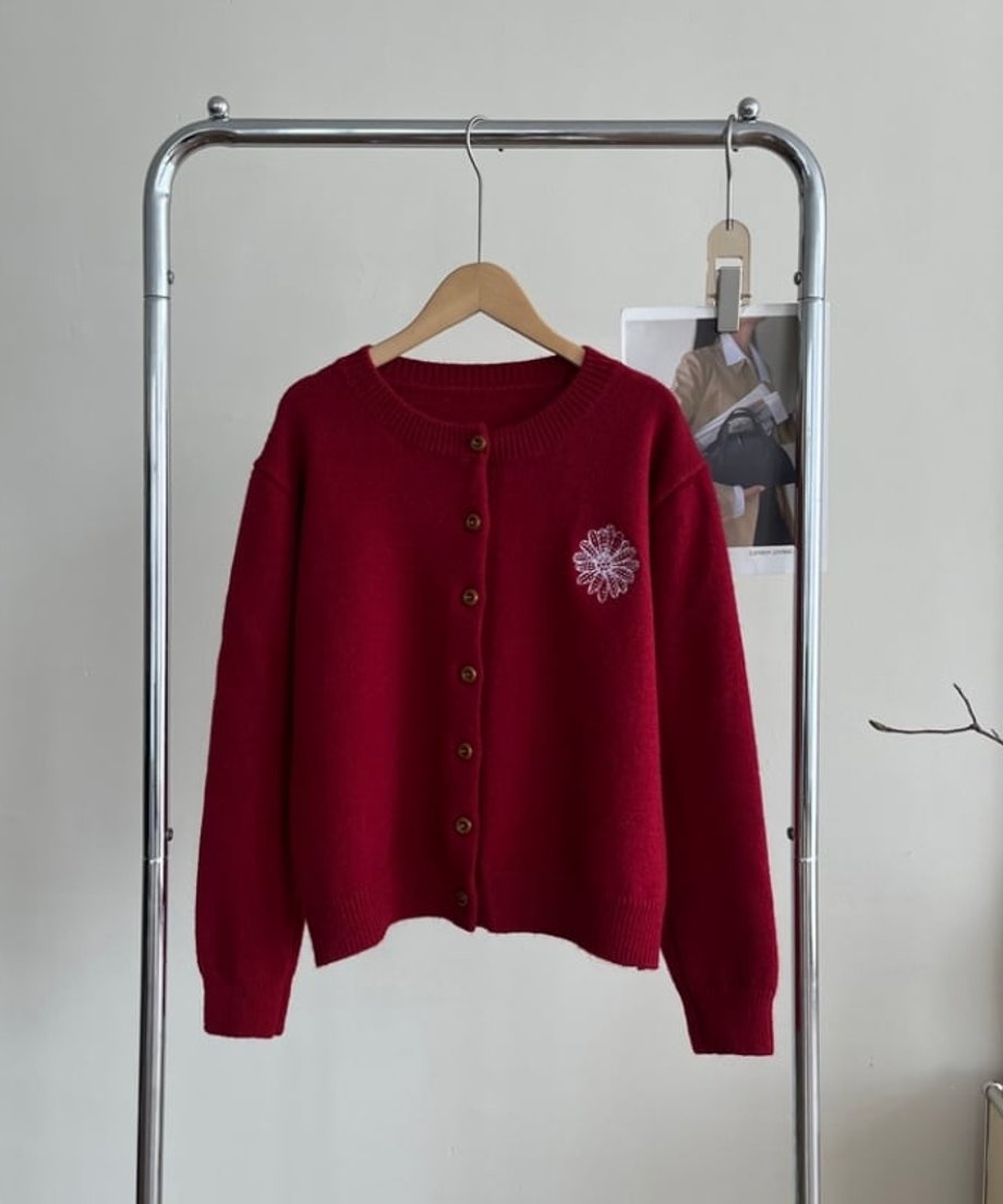 レッドの花柄刺繡ニットカーディガンをハンガーにかけた状態。左胸に白い花柄刺繍があり、リブ編みの裾と袖口が特徴。