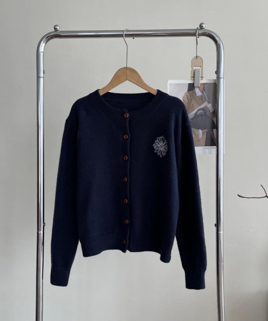 ネイビーの花柄刺繡のニットカーディガンをハンガーにかけた全体画像。クルーネックで、茶色のボタンと左胸の花柄刺繍が視認できる。