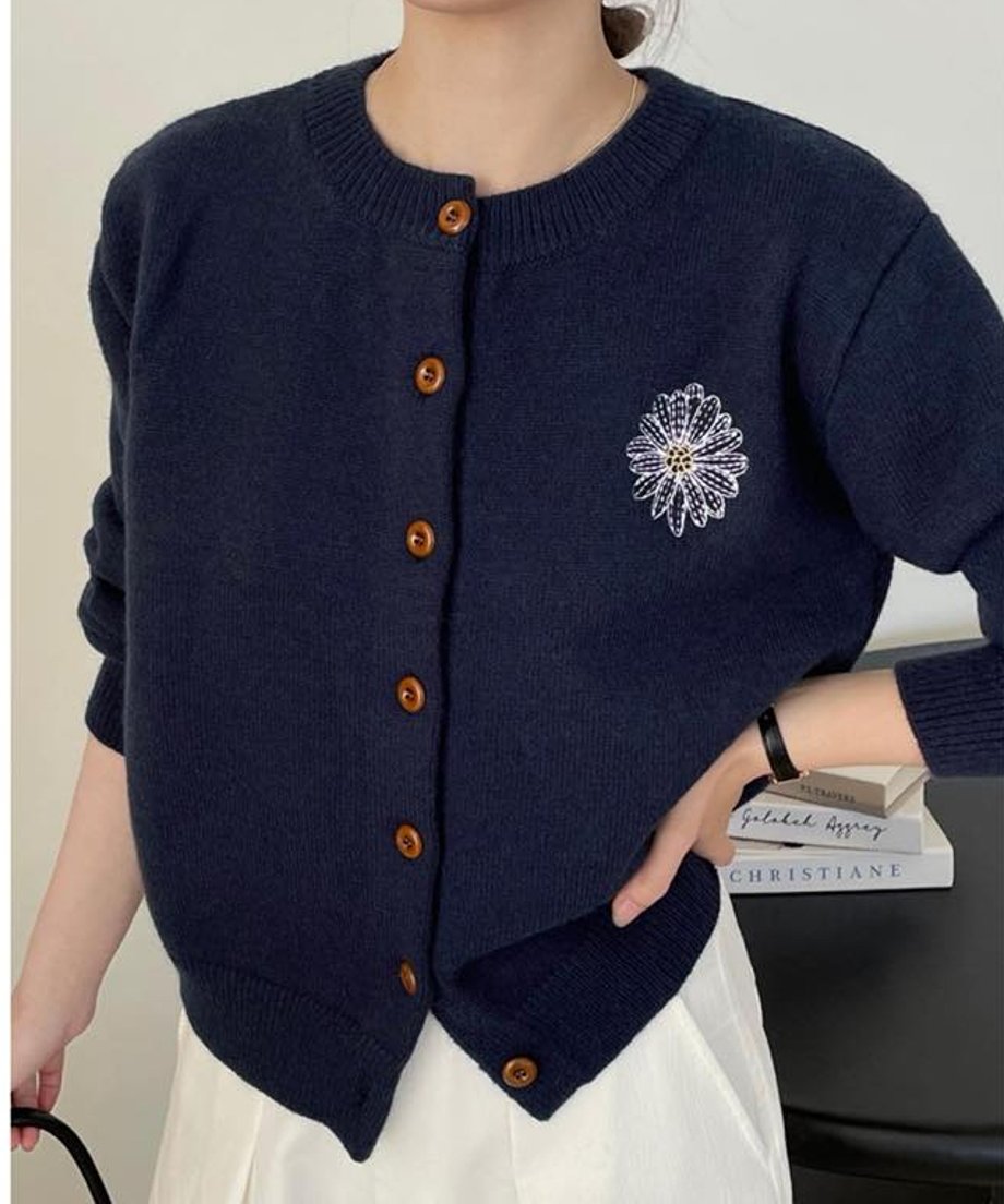 ネイビーの花柄刺繡ニットカーディガンの胸元とウエスト部分のクローズアップ。白い花柄の刺繍と丸い茶色のボタンが確認でき、裾はV字型にカットされている。