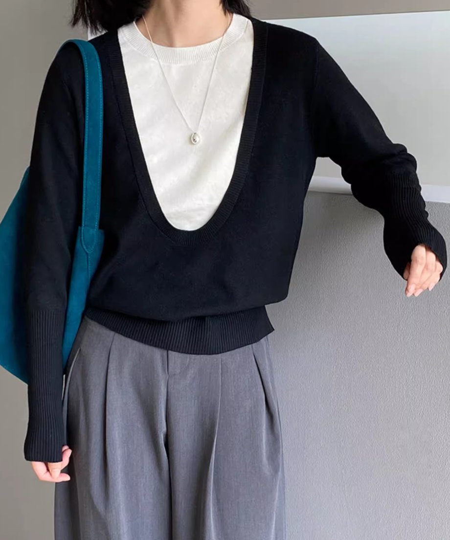 ブラックのディープUネックニットを着用した女性の半身像。白いTシャツをインナーに重ね、グレーのワイドパンツを着用。袖口のリブ編みが強調されている。