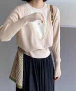 アプリコットのディープUネックニットを着用した女性の半身像。白いTシャツをインナーに重ね、黒いスカートを着用し、柄のスカーフを腰に巻いている。