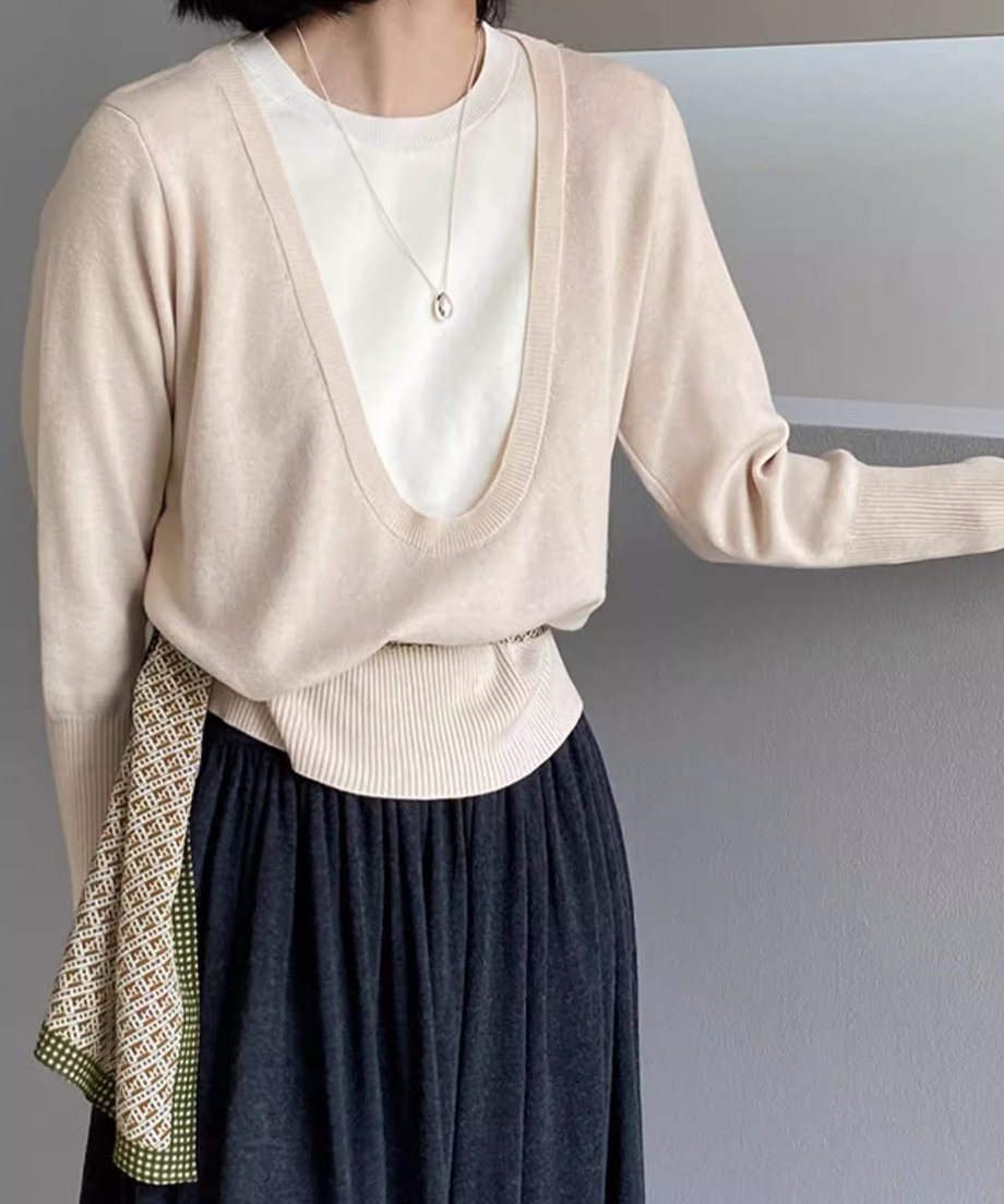 アプリコットのディープUネックニットを着用した女性の半身像。白いTシャツをインナーに重ね、黒いロングスカートと、柄のスカーフを着用。