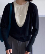 ブラックのディープUネックニットを着用した女性の胸元アップ。白いTシャツをインナーに重ね、シルバーのロングネックレスを着用し、青いバッグを肩にかけている。