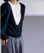 ブラックのディープUネックニットを着用した女性の半身像。白いTシャツをインナーに重ね、グレーのワイドパンツを着用し、青いバッグを持っている。