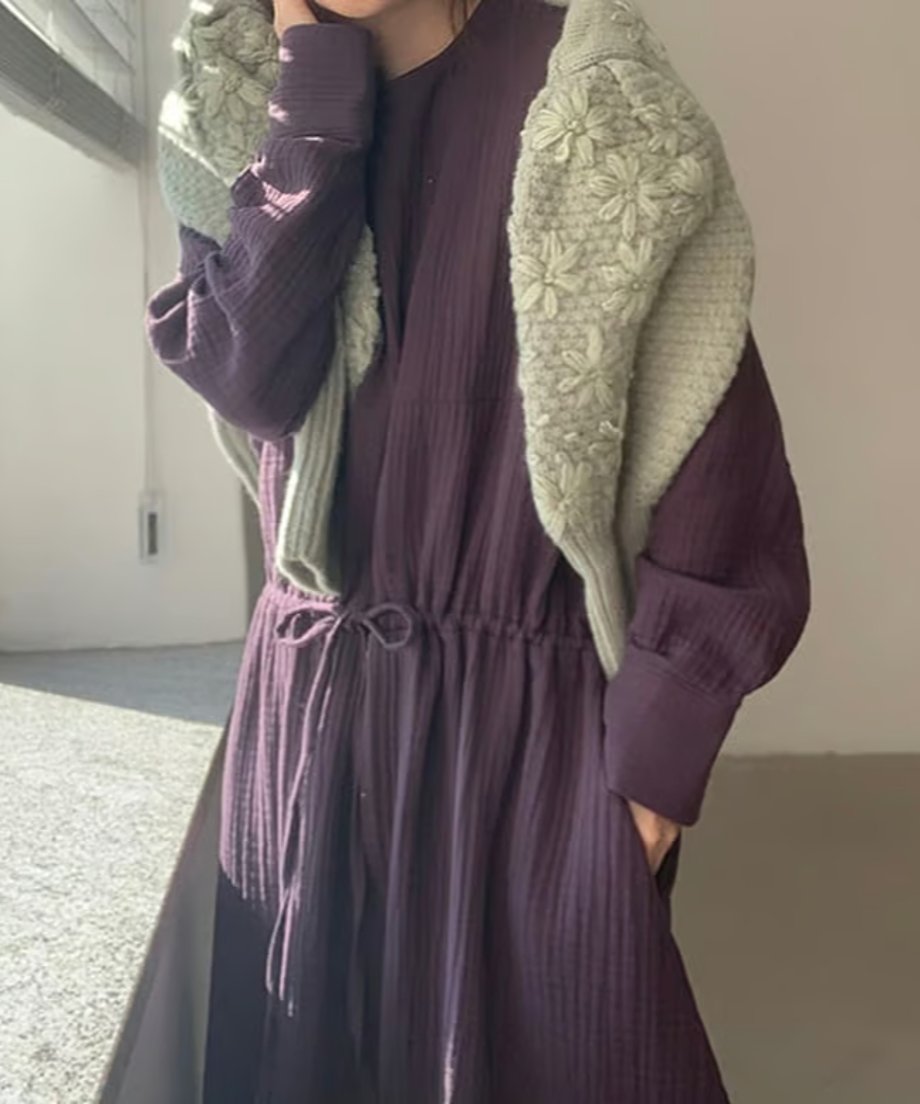 グリーンのフローラル刺繍セーターを肩にかけた女性、深い色のワンピースとコーディネート。