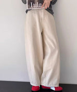 アイボリーのワイドパンツとチャコールグレーの長袖Tシャツを着た女性が座って雑誌を持っているクローズアップ写真。