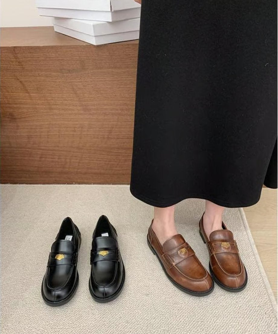 黒とブラウンの2色のコインモチーフ付きローファーが並べられた商品画像。着用者はブラウンを履いており、黒のロングスカートの裾が見えている。
