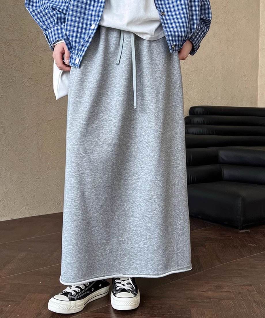 杢グレーのスウェット素材のロングスカートと青と白のチェック柄のトップス、白いTシャツを重ね着した人物が、スニーカーを履いている全身ショット。ウエストのドローコードが見える。