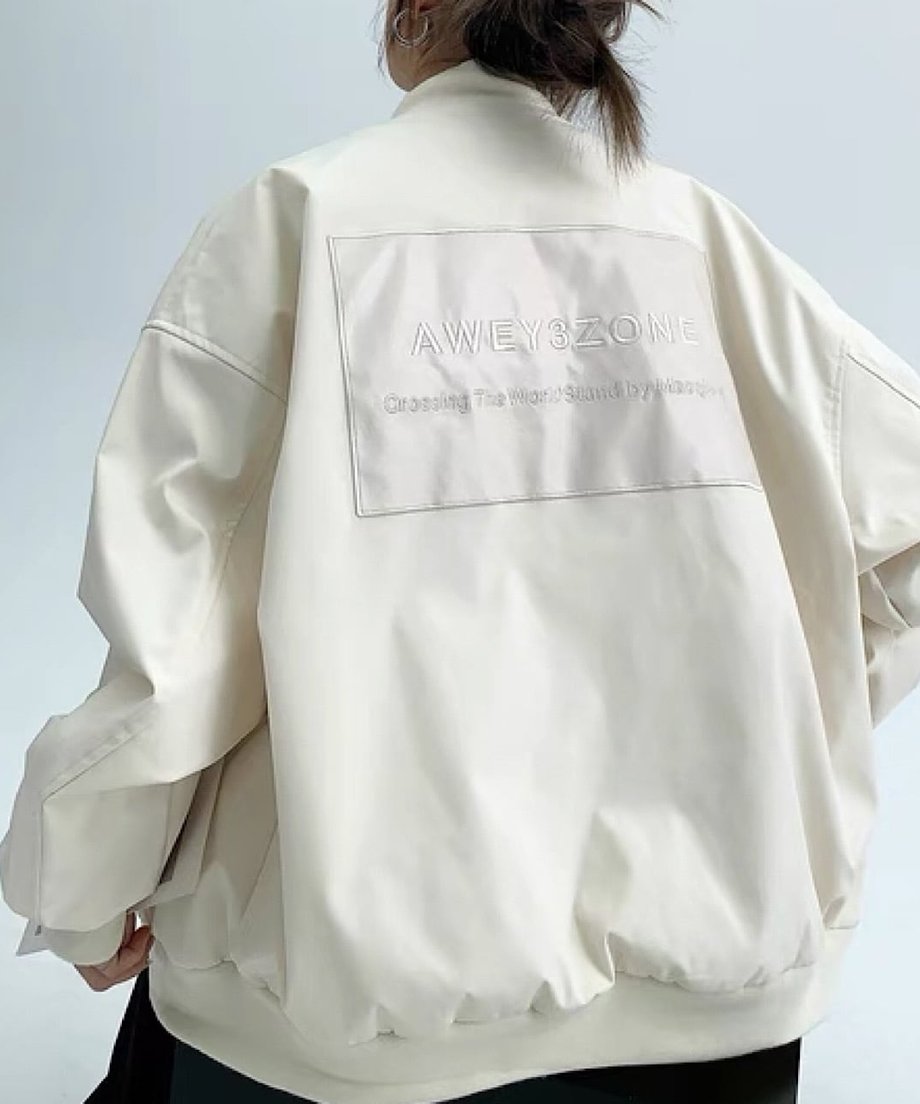 オフホワイトのオーバーサイズボンバージャケットを着用した後ろ姿。背中に同色系のロゴ刺繍パッチが施されている。