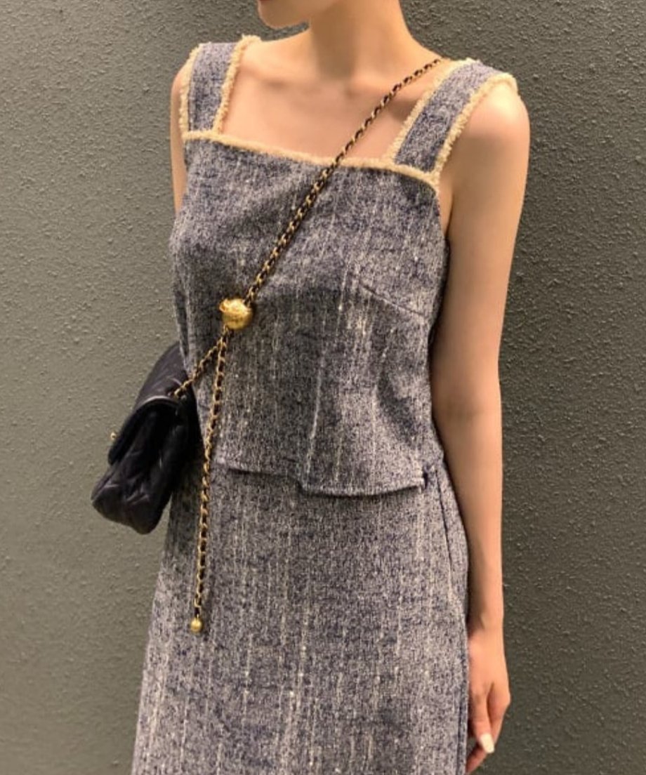 ブルーのツイードセットアップを着用した女性の上半身のクローズアップ。チェーンバッグを合わせている。