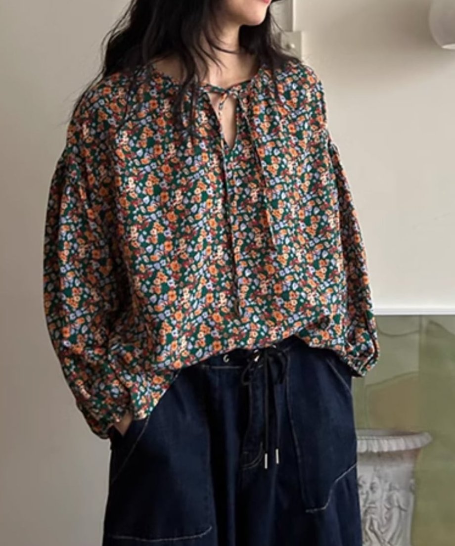 花柄のVネックブラウスと濃紺のドローコード付きワイドデニムパンツ、ブラウンのシューズを着用した女性が、正面を向いて立っている全身コーディネート画像。
