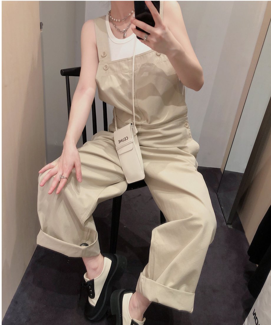 カーキのオーバーオールを着用した人物が椅子に座って足を崩している。