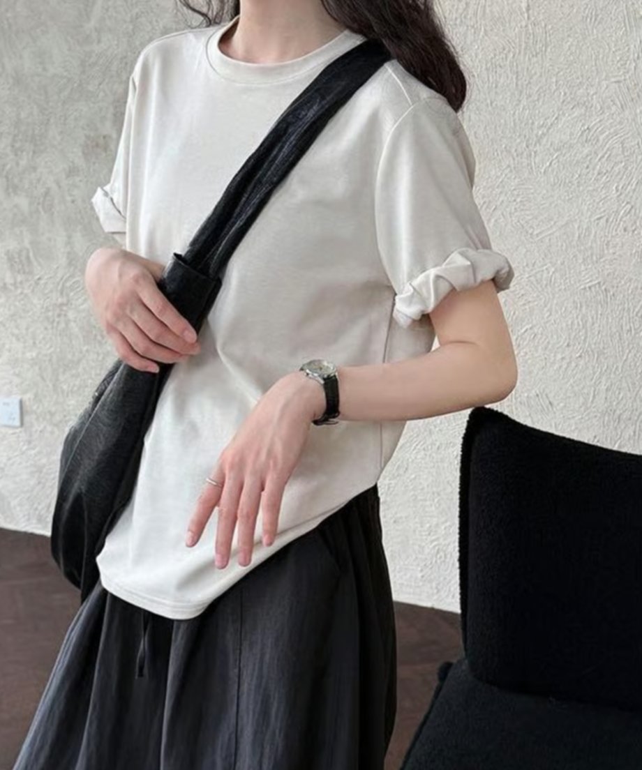 ベージュのTシャツと黒のショルダーバッグを合わせたシンプルな着こなし