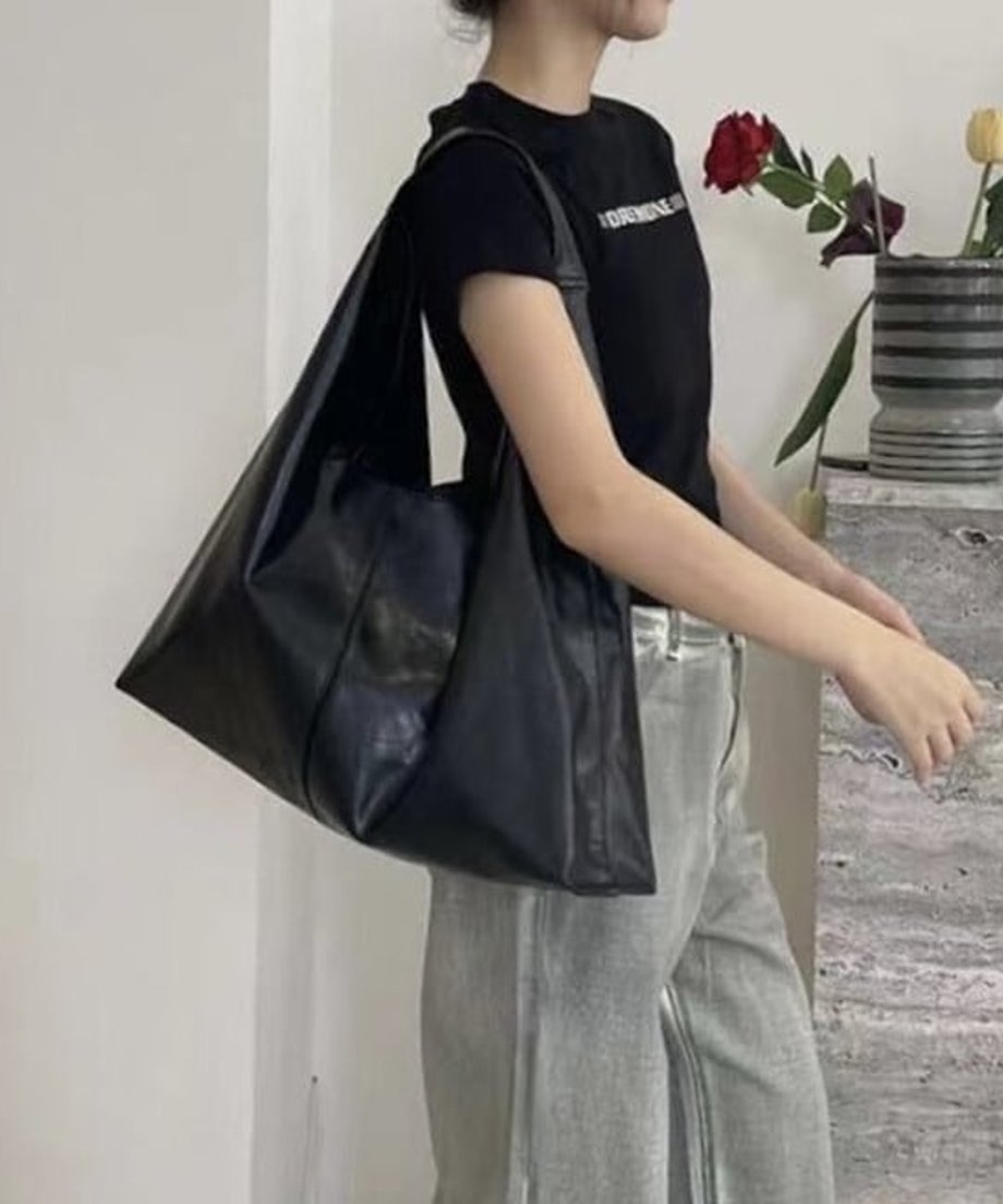 黒いTシャツとグレーのワイドパンツを着用した女性が、マットな質感の黒のソフトPUレザー製ショルダーバッグを肩に掛けている写真。