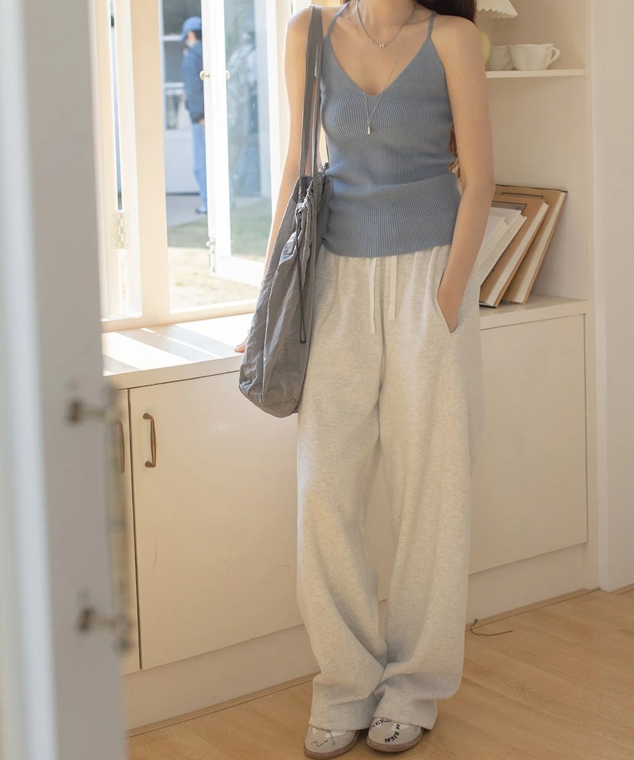 ブルーグレーのリブ編みVネックキャミソールを着用した女性。白のスウェットパンツと合わせた女性に窓から日差しが入っている写真。