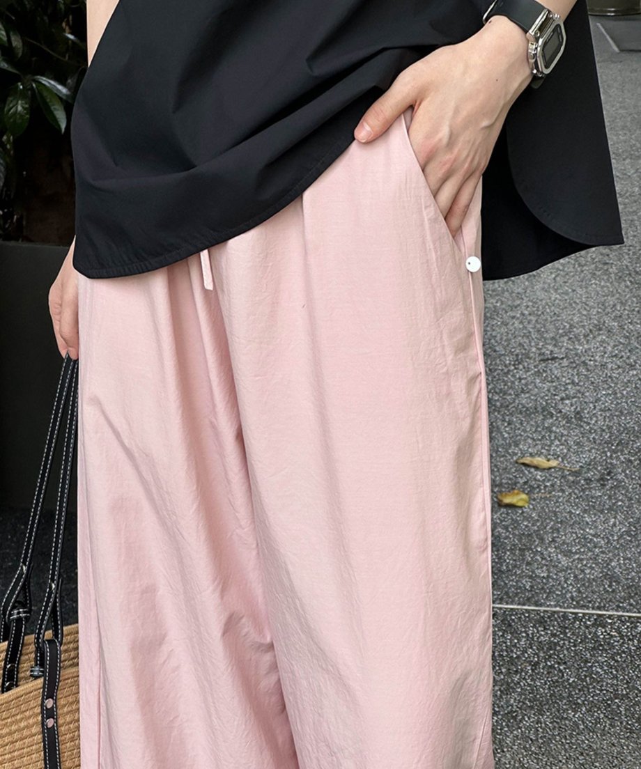 ピンクのワイドレッグパンツのウエスト部分とポケットディテール（白いボタン付き）に焦点を当てたクローズアップ写真