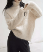 アプリコットの毛足の長いニットと、黒っぽいストレートワイドパンツを合わせた女性の写真。