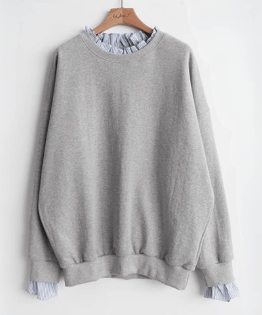 グレーのレイヤードスウェットをハンガーにかけた正面の商品画像。フリルの付いたブルーストライプのネックと袖口が特徴。