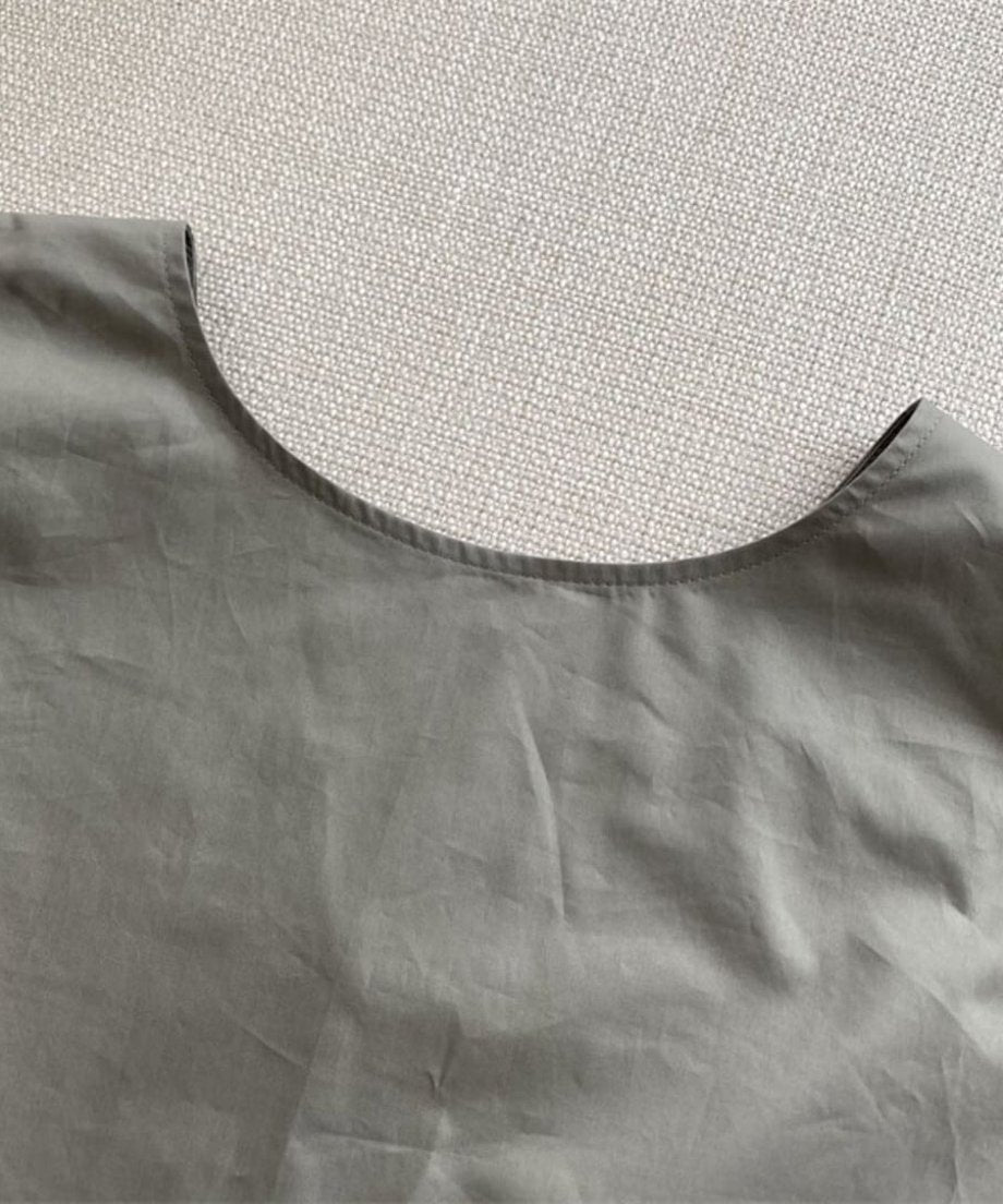 グレーの生地のラウンドネック部分のアップ。丁寧なステッチとナイロン特有の質感がわかる詳細。