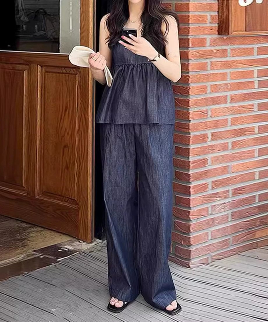 デニムセットアップを着用し、レンガの壁の前に立つ女性のスタイリッシュな全身写真。
