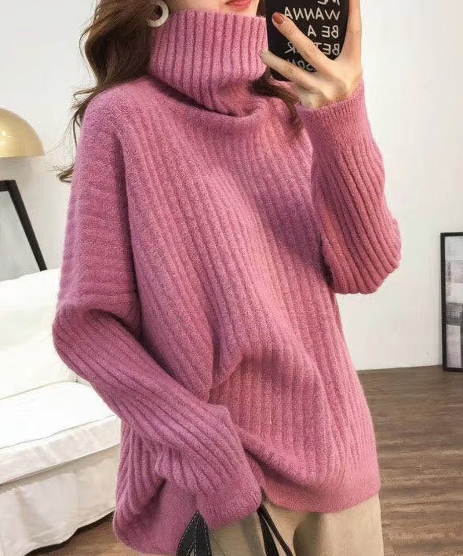 ピンクのオーバーサイズタートルネックニットを着用した女性の上半身。太めのリブ編みとルーズな袖口が特徴。