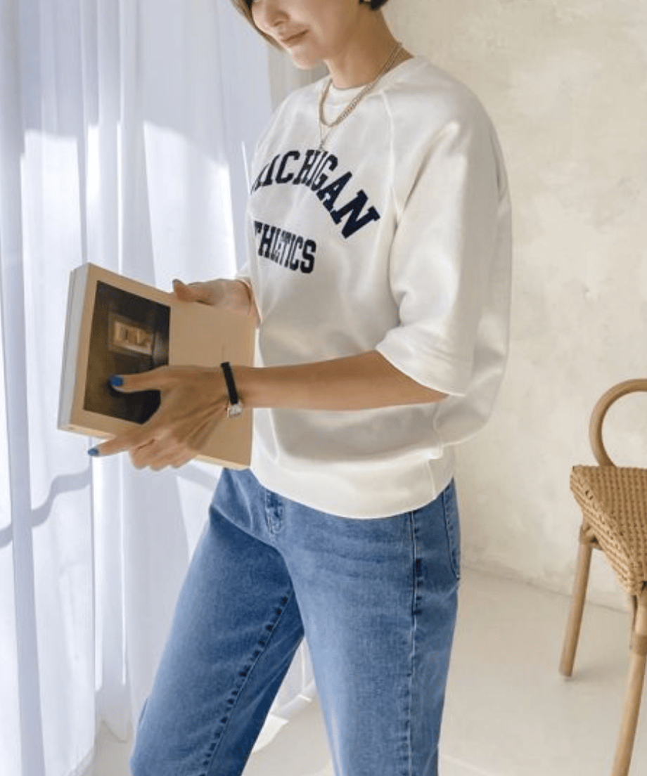 ホワイトロゴTを着た女性が窓際で本を読んでいる姿。