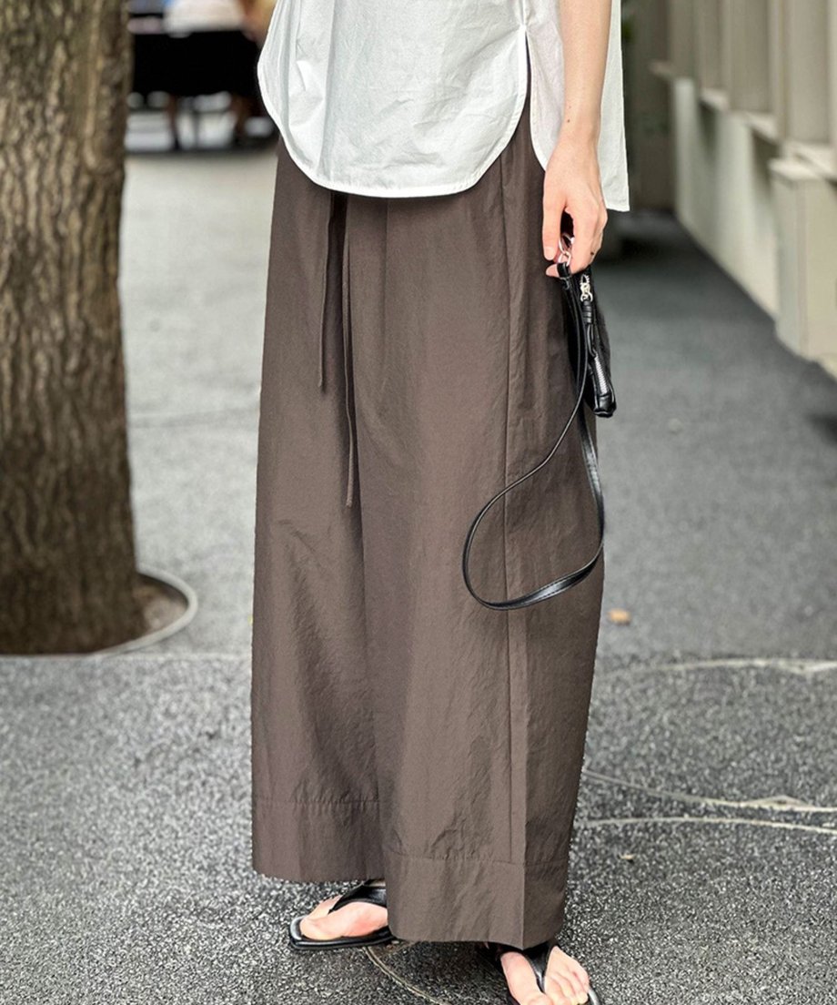 ブラウンのワイドレッグパンツと白のブラウスを着用し、黒のミニショルダーバッグを持った、街中での全身写真