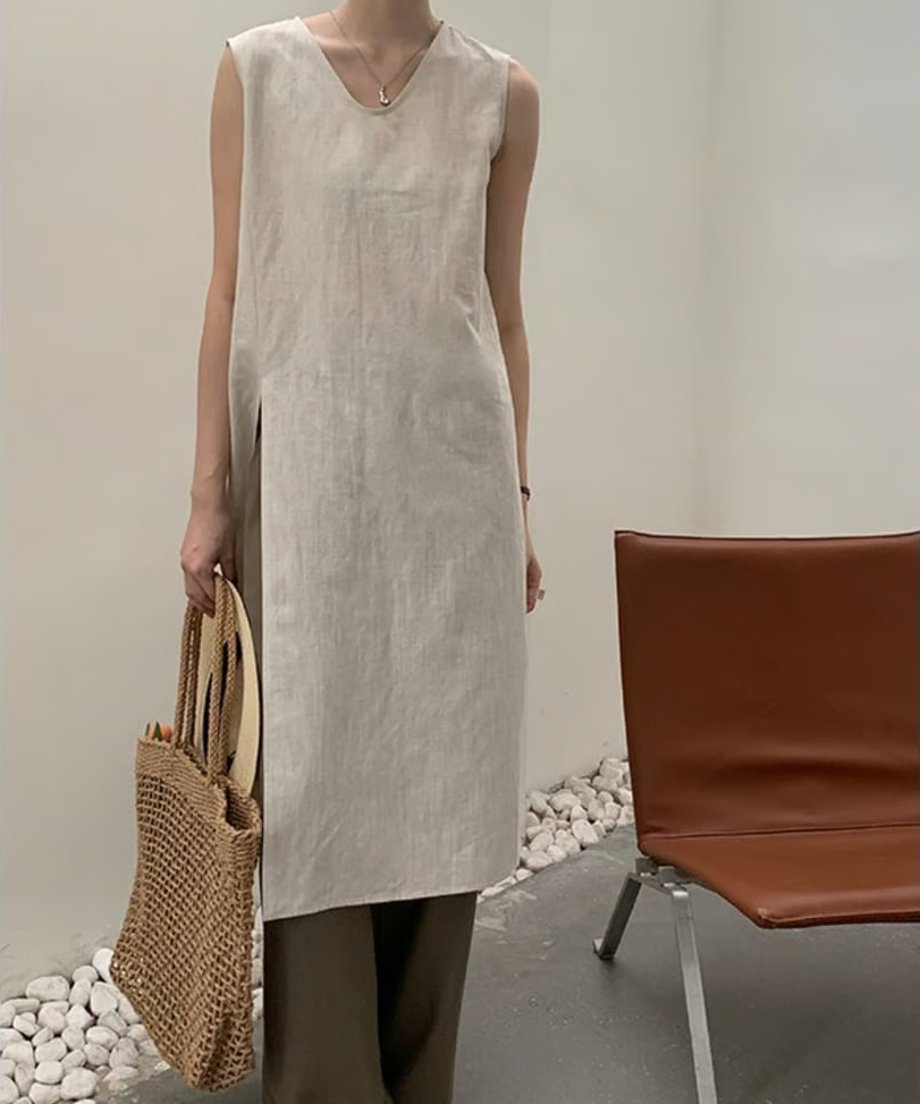 ベージュのノースリーブチュニックを着用し、カゴバッグを持った女性の正面からの立ち姿。