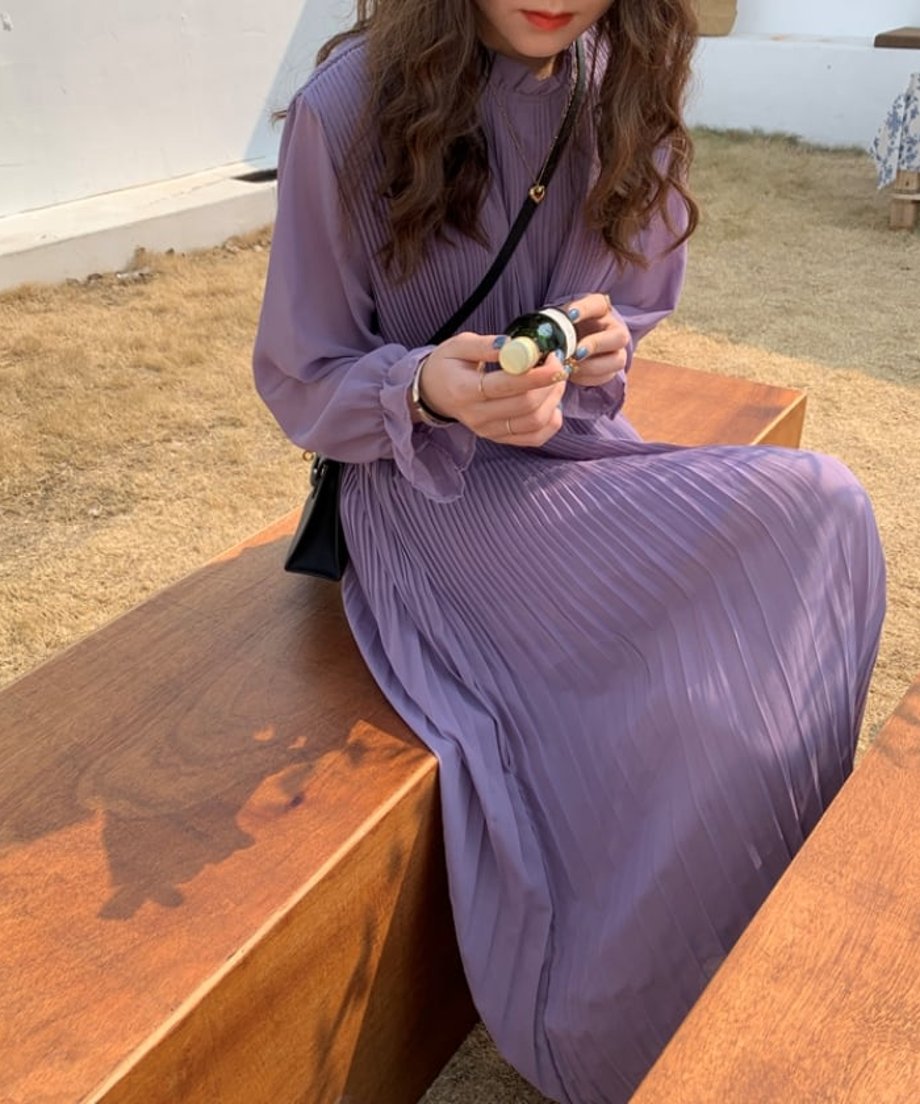 カフェで椅子に座り、プリーツが美しく広がるパープルワンピースを着用。